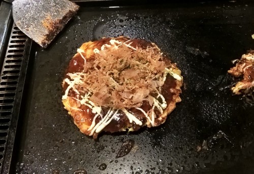 Photo d'un okonomiyaki, spécialité culinaire japonaise, sur sa plaque chauffante.