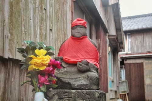 Jizo devant lequel est disposé un arrangement floral dans les ruelles d'Ojika