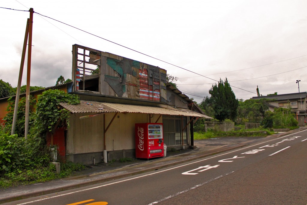 A road and abandoned building being slowly consumed by nature on the island of Sakurajima.