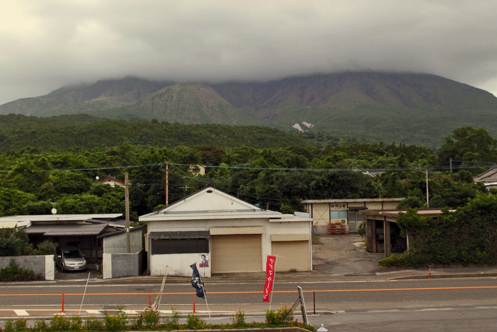 Clouds covering the volcano and surrounding nature at the island of Sakurajima with a house and road at the front..