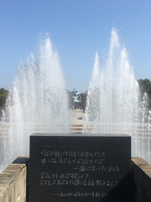 Black stone sign with water gushing from the fountain behind it at Nagasaki Peace Park.